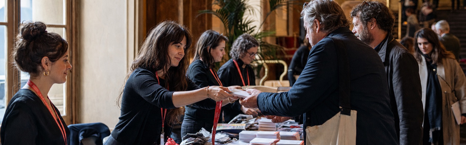 I volontari consegnano badge stampati e programmi al banco accrediti del festival.
